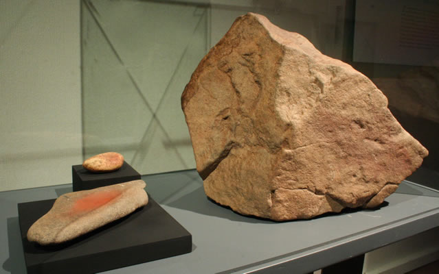 a) Bloque con pictografía estilo El Médano,cetáceo con balsero. Pescadores Tardíos. Colección Museo Augusto Capdeville, Taltal. b) Mortero y mano de moler con pigmento rojo.Piedra y óxido de fierro. Costa de Taltal. Pescadores Tempranos f Tardíos. Colección Museo Augusto Capdeville, Taltal.