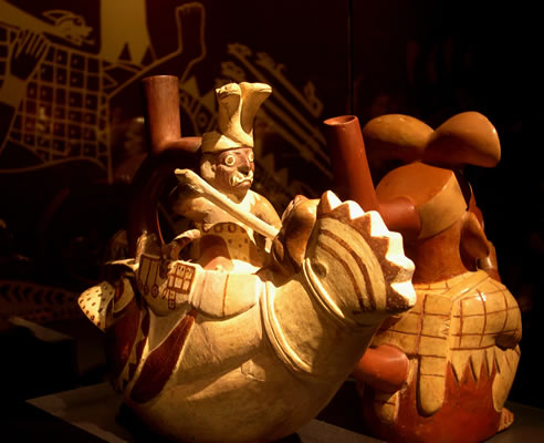 Botella asa-estribo: «Cara Arrugada» navegando sobre embarcación en forma de pez mítico junto a prisioneros amarrados y con soga al cuello. Museo Larco, Lima – Perú