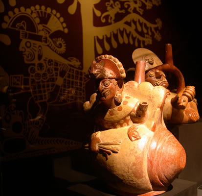 Botella asa-estribo: «Cara Arrugada » con tocado de felino y cuerpo de concha Strombus , portando estólica y dardos. Museo Larco, Lima – Perú